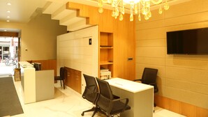 A modern reception area with a reception desk, two office chairs, a chandelier, and a flat-screen TV on the wall. - Hotel Reva Regency (Bhopal)