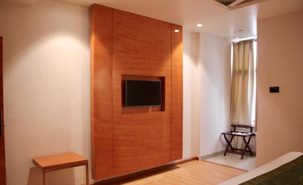 Una habitación moderna con una pared de acento de madera, un televisor de pantalla plana, una pequeña mesa de madera y una ventana con cortinas.
