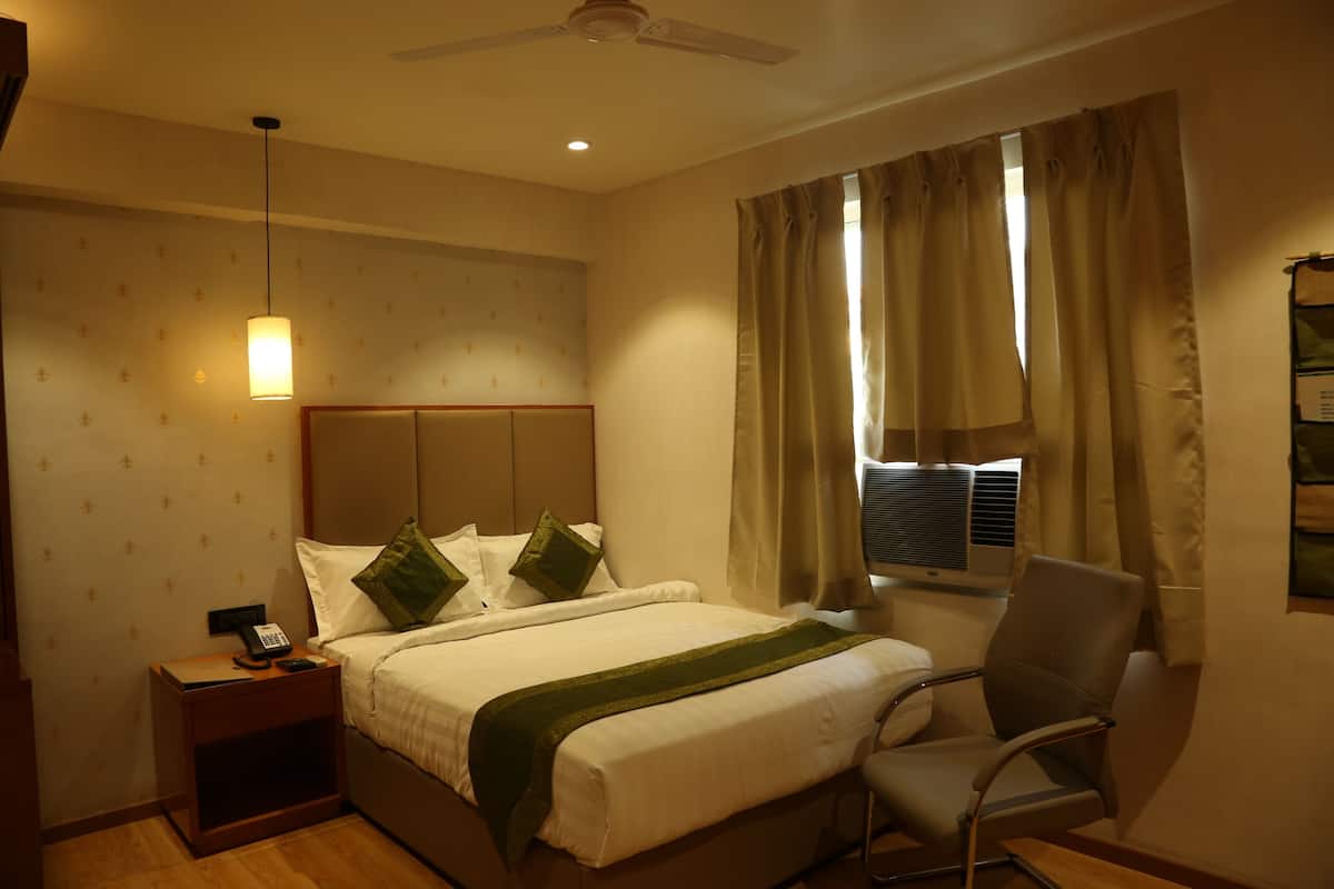 Quarto de hotel com cama, mesa de cabeceira, cadeira e janela com cortinas.