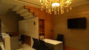 A modern office space with a desk, two office chairs, a bookshelf, a television, and a staircase. - Hotel Reva Regency (Bhopal)