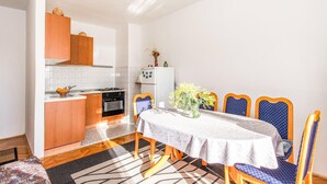 Une cuisine compacte équipée d’une cuisinière, d’un four et d’un réfrigérateur blanc. Une table à manger recouverte d’une nappe blanche et entourée de chaises bleues est dressée pour quatre personnes.