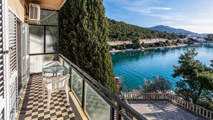 Un balcon doté d’un sol à carreaux, d’une table et de chaises, offrant une vue sur un lac où naviguent des bateaux et sur un paysage vallonné.