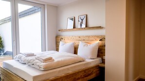 A bedroom with a wooden bed frame, white bedding, and a large window. - "Pure relaxation: your exceptional vacation apartment in Winterberg!" (Winterberg)