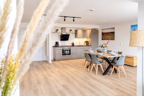 A modern kitchen with a dining area, wooden flooring, and a view of a landscape painting.