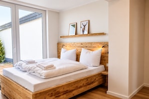 A bedroom with a wooden bed frame, white bedding, and a large window.