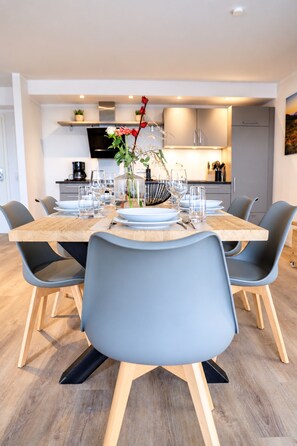 A modern dining area with a wooden table, grey chairs, and a vase with flowers.