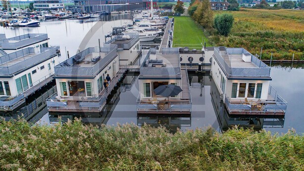 A marina with multiple houseboats docked in calm water, featuring outdoor seating areas and a grassy path nearby. - Stunning ship in Aalsmeer with kitchen (Aalsmeer)