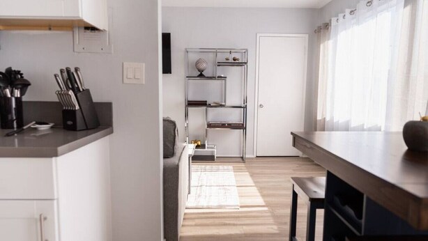 Eine moderne Küche mit weißen Schränken, einer Arbeitsplatte mit Messern, einem Holzboden und Blick auf eine weiße Tür.