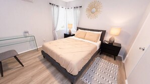 Ein modernes Schlafzimmer mit Bett, Nachttischen, einem Glastisch, einer Bank und einem gemusterten Teppich.