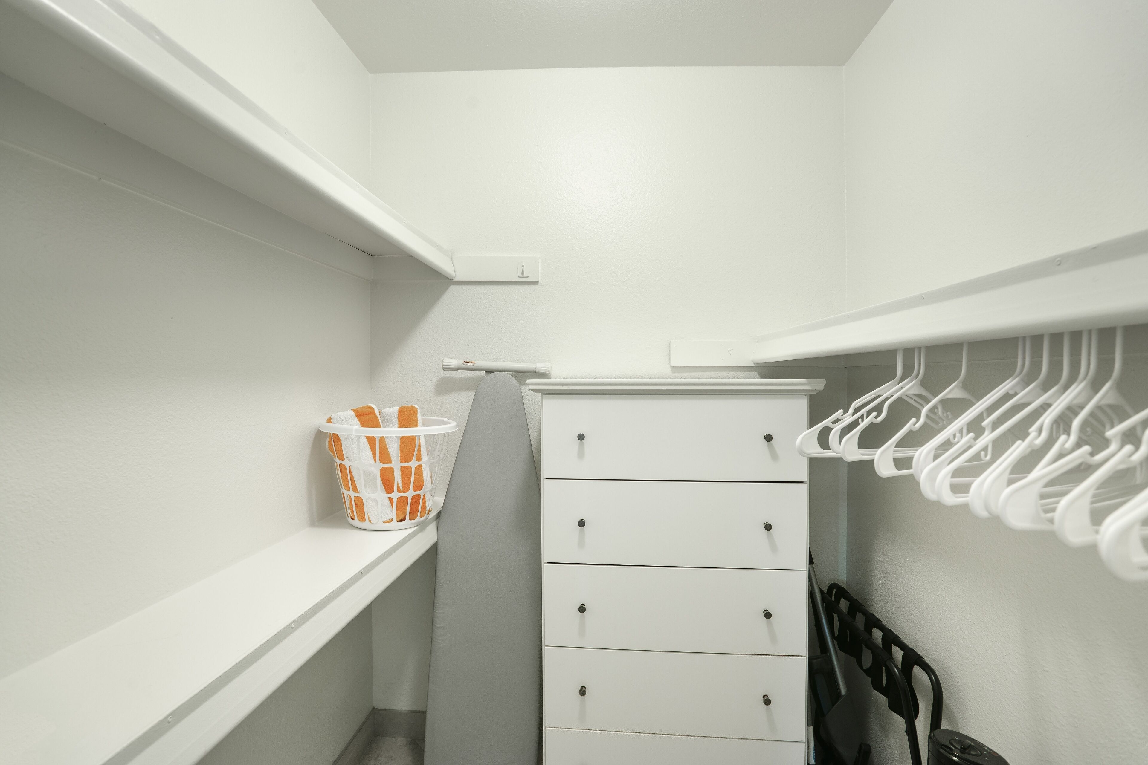 A white closet with a hanging rack and a storage cabinet.