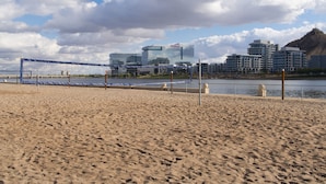 A beach volleyball court with a net, a sandy beach, and a cityscape in the background including modern buildings and a hill. - 238- Fully Furnished with WiFi by RedAwning (Scottsdale)