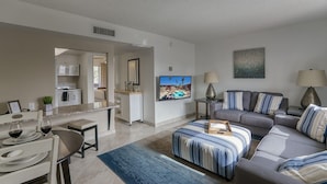 A modern living room with a grey sofa, a striped ottoman, and a television mounted on the wall. - 141 Fully Furnished Condo by RedAwning (Scottsdale)