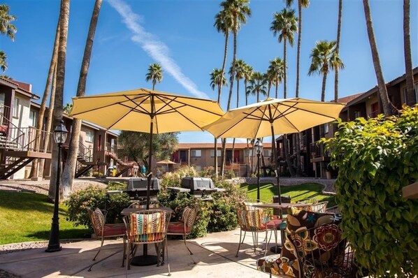 An outdoor patio with yellow umbrellas, wicker chairs, and a grill.