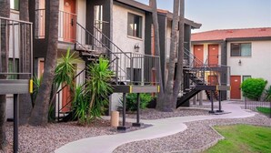 A multi-story building with external staircases, palm trees, and a gravel pathway. - 141 Fully Furnished Condo by RedAwning (Scottsdale)