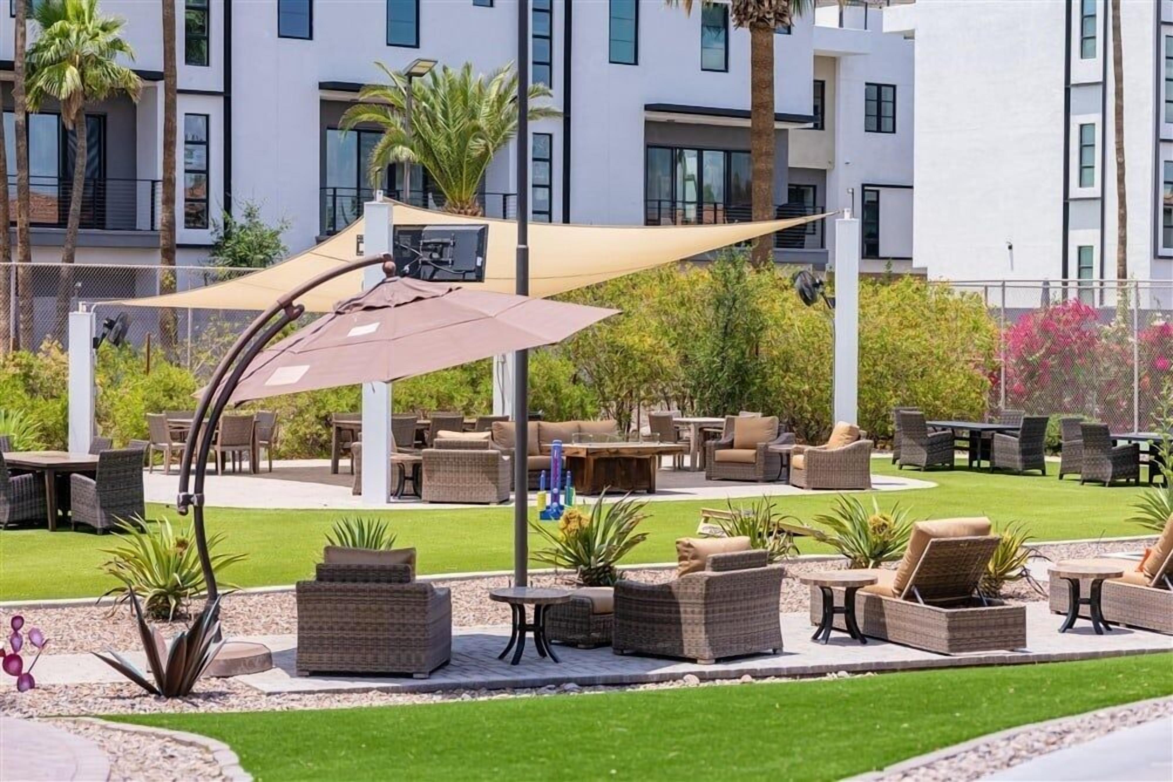 Area patio esterna con mobili in vimini, un ombrellone grande e vista su un edificio moderno sullo sfondo.