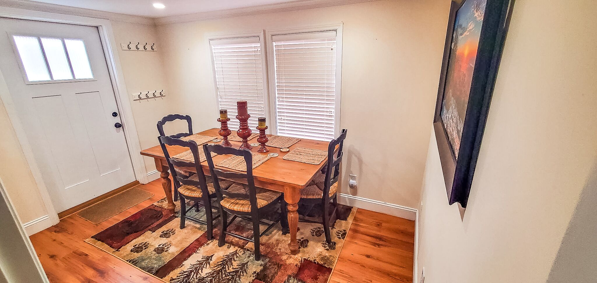 Un comedor con una mesa de madera, cuatro sillas, un tapete y un cuadro en la pared.