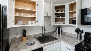 Una cocina con armarios blancos, encimera de granito, estufa negra y microondas.