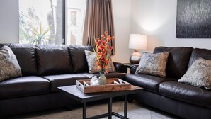 Una sala de estar moderna con un sofá de cuero, una mesa de centro de madera con objetos decorativos y vistas a través de un ventanal.