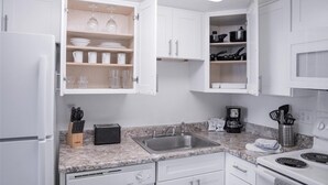 A modern kitchen with white cabinetry, a granite countertop, a built-in sink, and a microwave.
