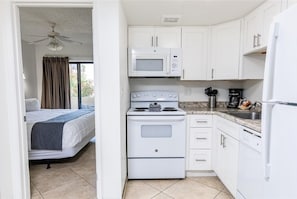 Una cocina compacta con gabinetes blancos, microondas, estufa y refrigerador.