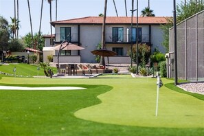 Un parcours de golf avec un green d’entraînement, un espace de détente avec des meubles d’extérieur, et un bâtiment à deux étages avec un toit rouge en arrière-plan.