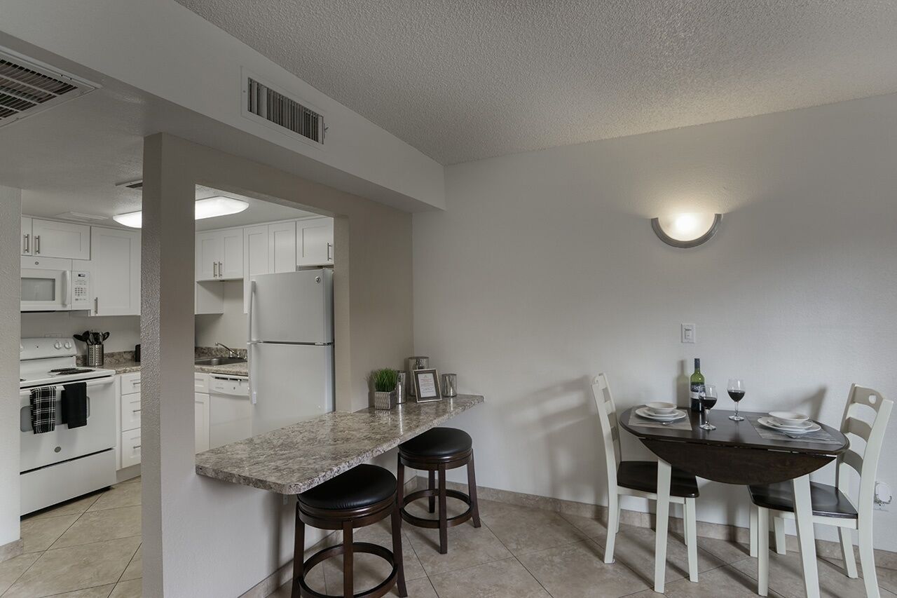 Eine moderne Küche mit weißen Schränken, einer Arbeitsplatte aus Granit und einem Essbereich mit einem dunklen Holztisch und weißen Stühlen.