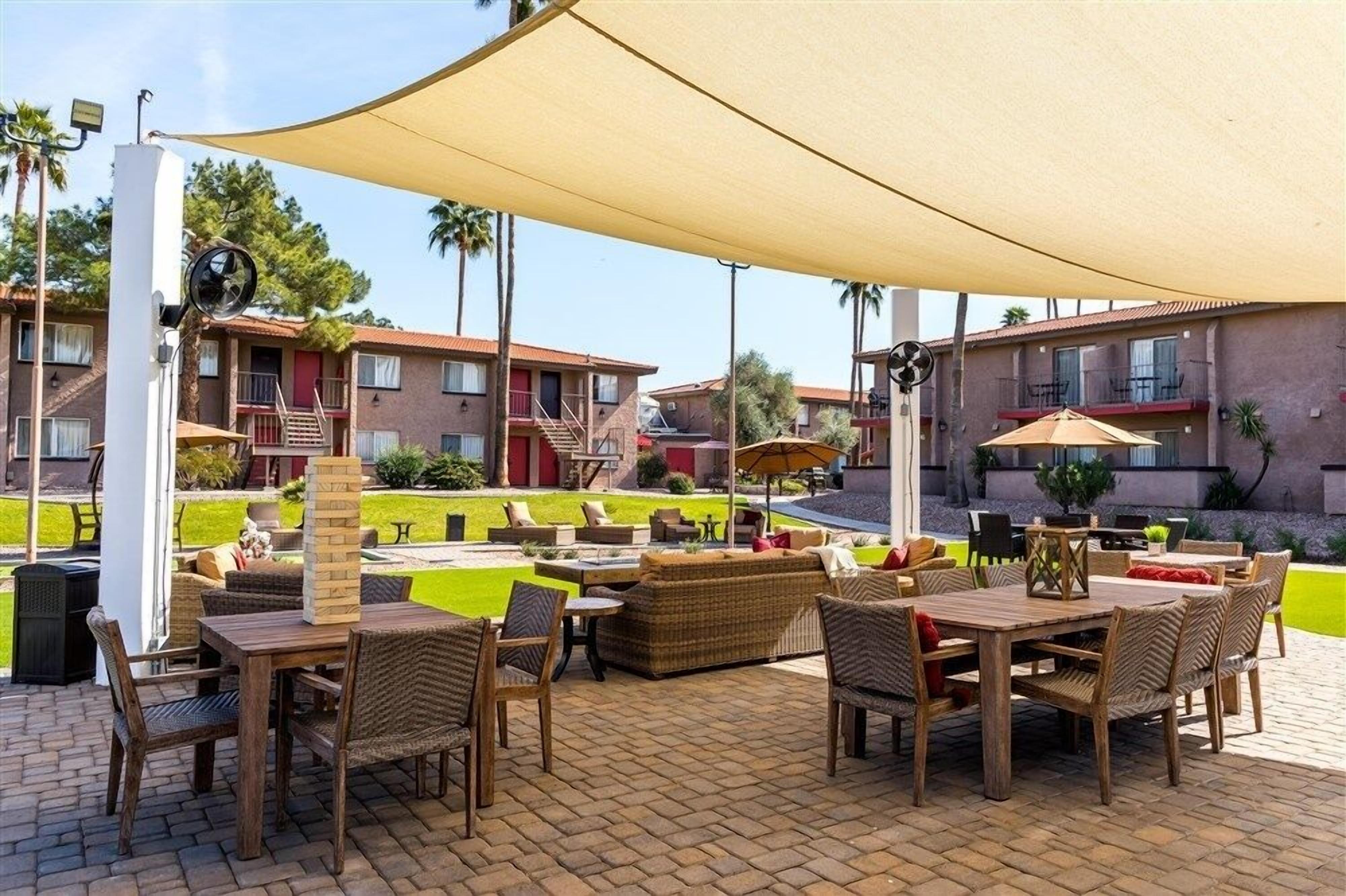 Un patio al aire libre con mobiliario de mimbre, un paraguas grande y una piscina.