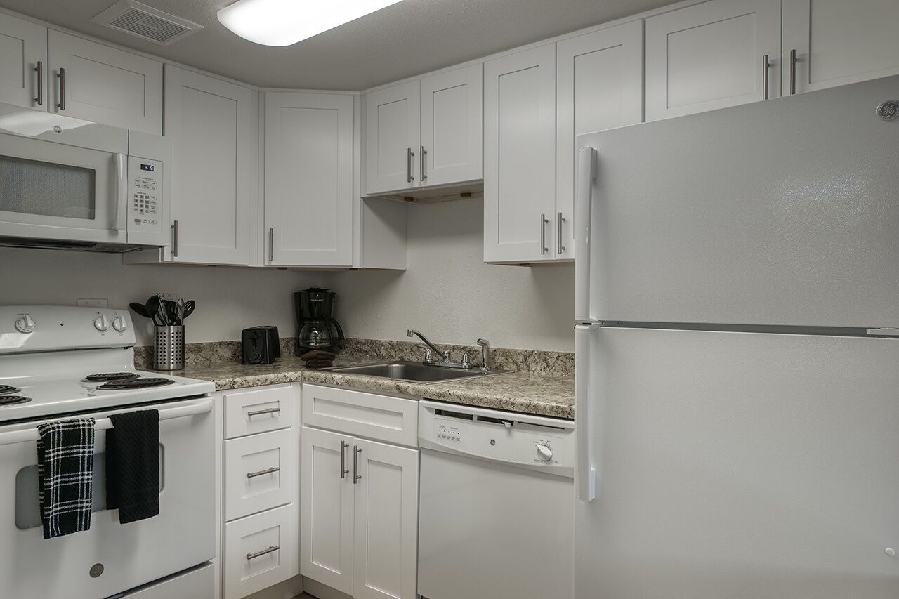 A modern kitchen with white cabinetry, a built-in microwave, a stove, a sink, and a refrigerator.