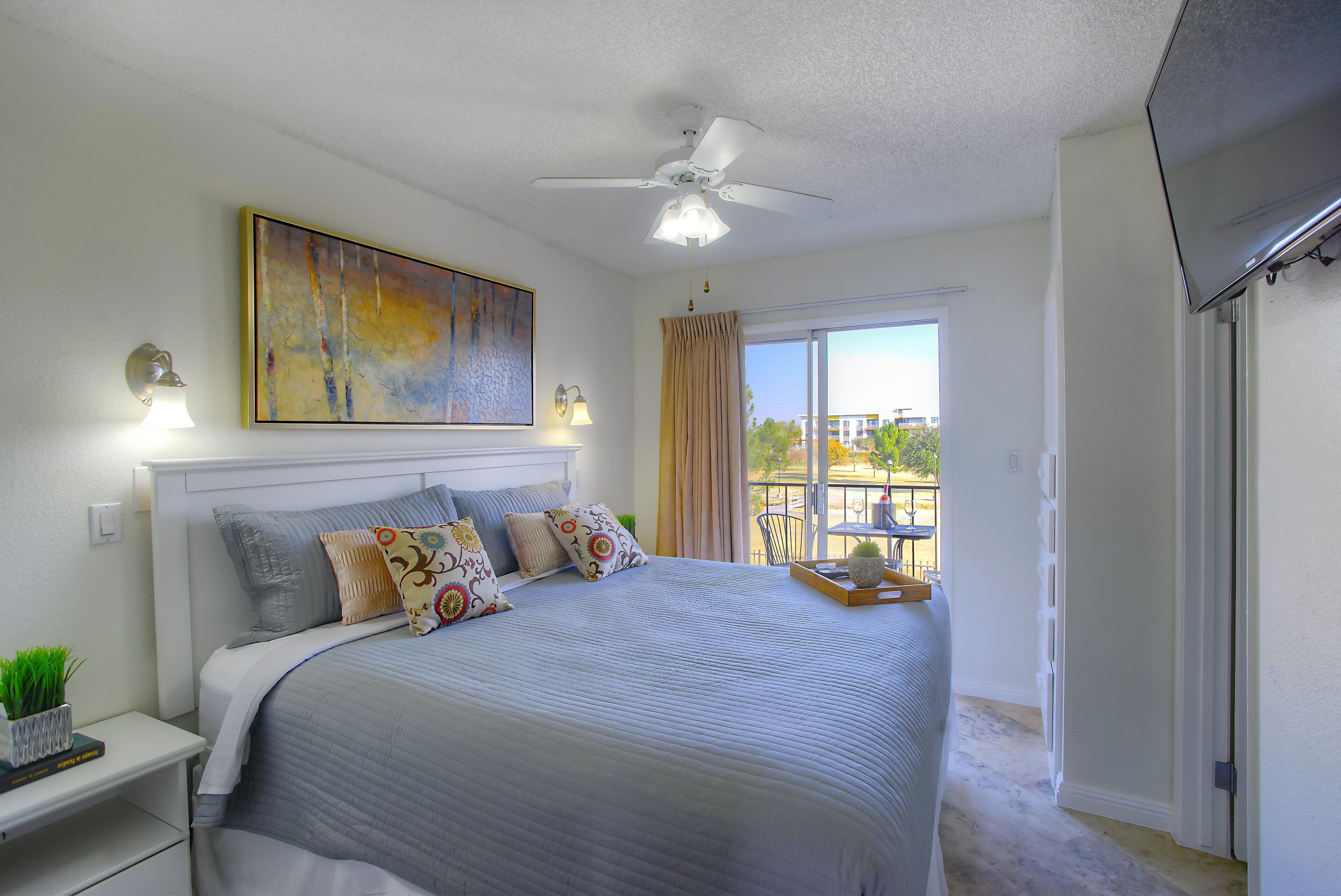 A bedroom with a bed, a ceiling fan, a window with curtains, and a view of the outside.