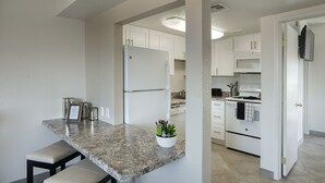 A kitchen with white cabinets, a granite countertop, a refrigerator, an oven, and a microwave.