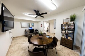 Cozy dining area with a round table and four chairs, a flat-screen TV, and a bookshelf.