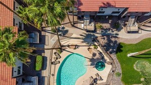 An aerial view of a resort with a swimming pool, palm trees, and a well-maintained lawn.
