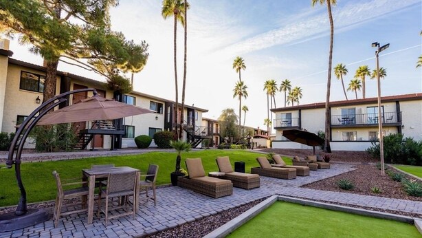 A courtyard with outdoor seating, palm trees, and a building with balconies.