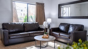 A modern living room with two leather sofas, a round coffee table, and a large mirror on the wall.