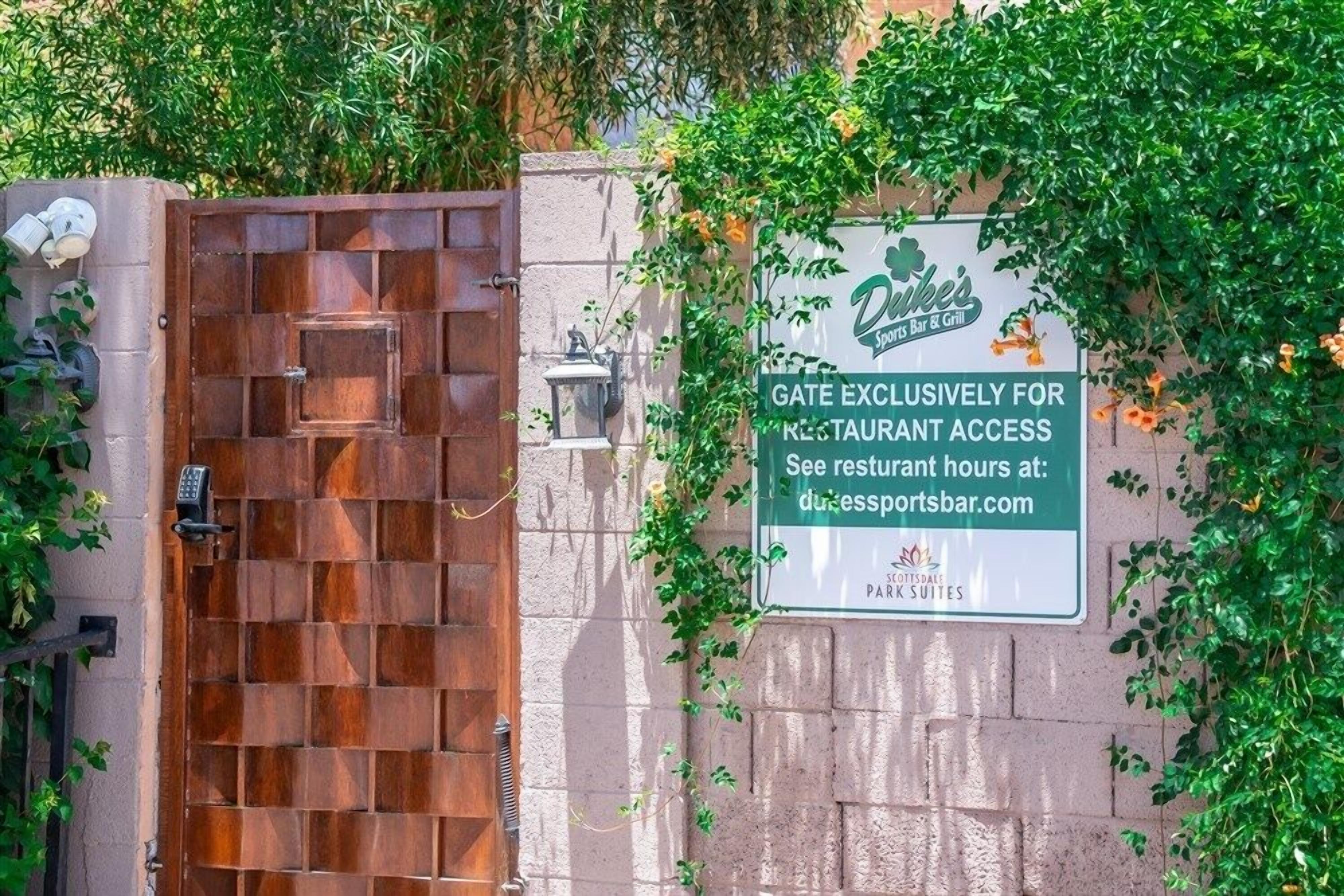 Une entrée fermée par un portail, avec un panneau indiquant l’accès au restaurant.