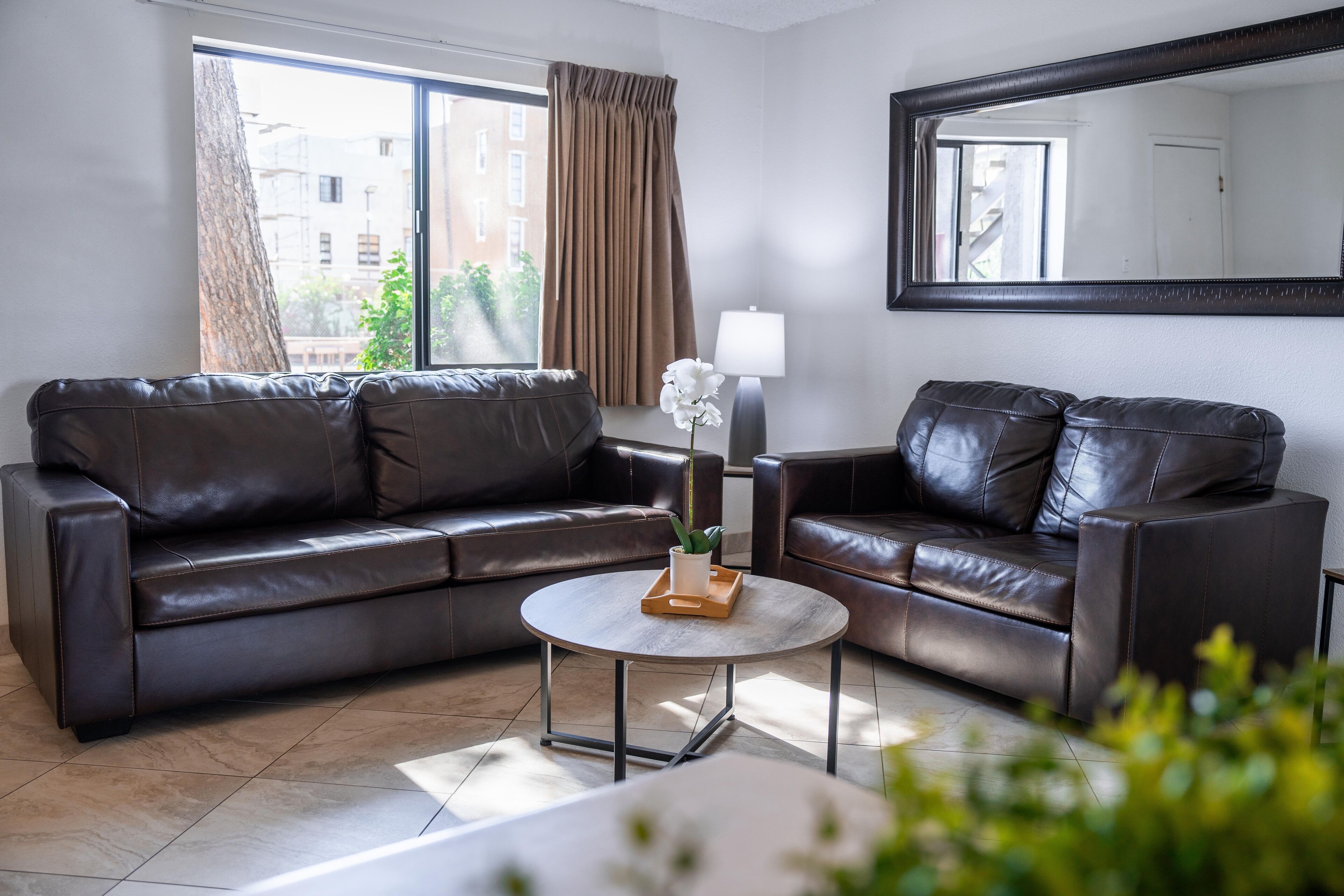 A modern living room with two leather sofas, a round coffee table, and a large mirror on the wall.