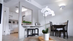 A modern kitchen with white cabinets, a welcome sign, and a dining area with a round table and chairs. - 109 Fully Furnished 1BR Suite-Prime Location! by RedAwning (Scottsdale)