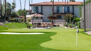 Um campo de golfe com putting green, uma área de areia e uma casa com varanda ao fundo.
