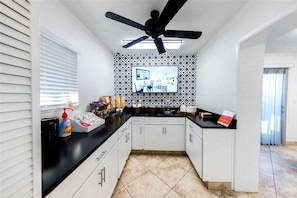 Una cocina moderna con armarios blancos, encimera negra y ventilador de techo.