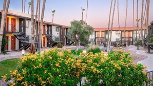 A hotel courtyard with multiple-story buildings, palm trees, and a central garden with yellow flowers. - Fully Furnished 1BR Suite-Prime Location! 110 by RedAwning (Scottsdale)