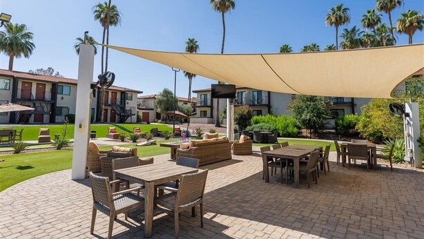 An outdoor patio area with wooden furniture, a large canopy, and palm trees. - Fully Furnished 1BR Suite-Prime Location! 110 by RedAwning (Scottsdale)