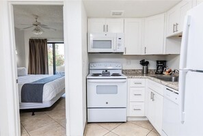A compact kitchen with a microwave, stove, and refrigerator, adjacent to a bedroom with a bed and curtains. - 209 Fully Furnished 1BR Suite-Prime Location! by RedAwning (Scottsdale)