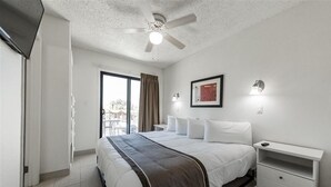 Een hotelkamer met een bed, een nachtkastje, een plafondventilator, een raam met gordijnen en een deur.