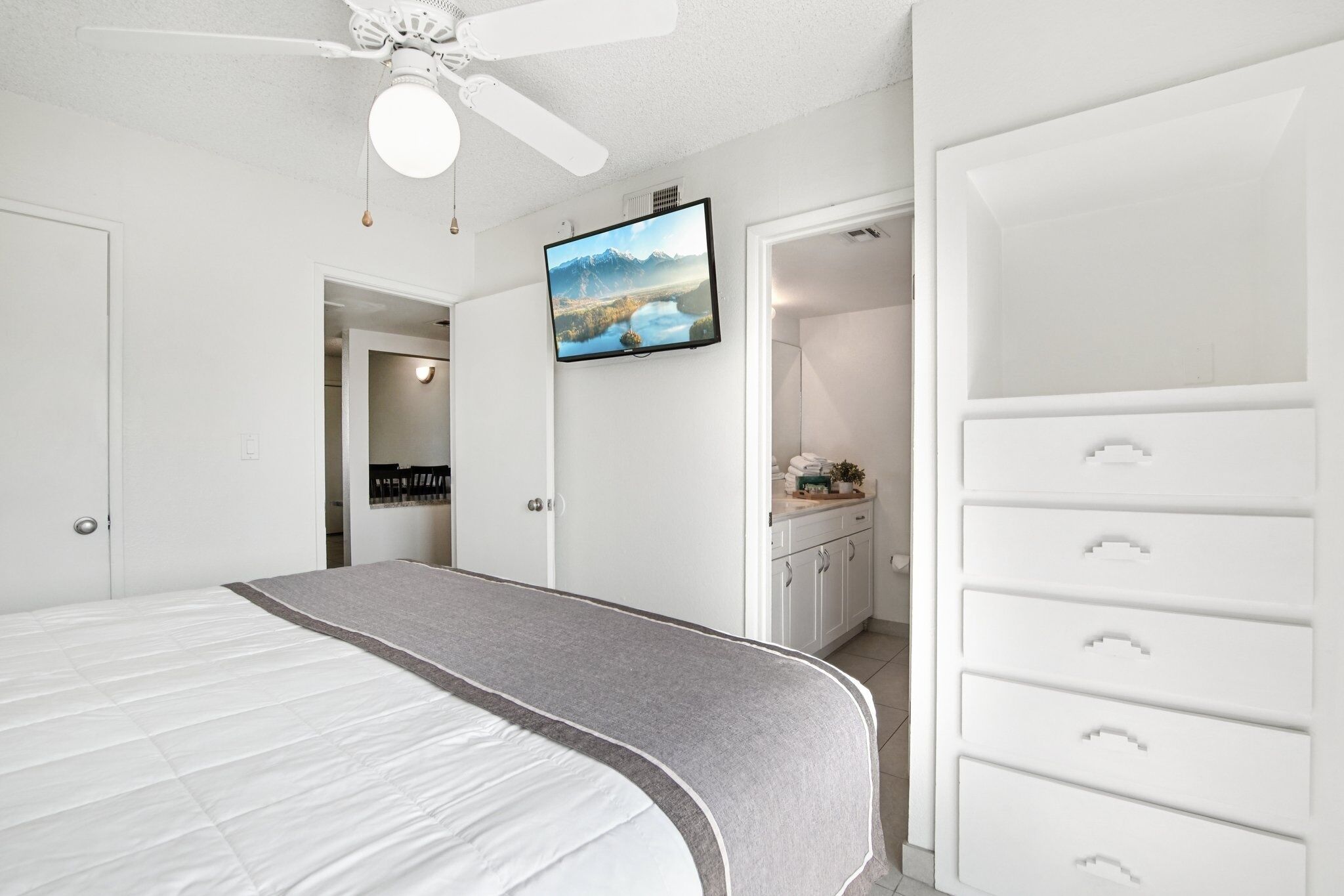 A bedroom with a bed, a ceiling fan, a TV, a dresser, and a closet.