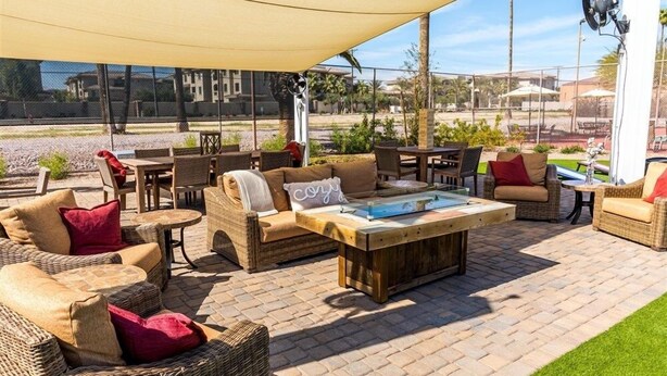 Eine Außenpatio-Terrasse mit Korbmöbeln, einem Holztisch und einem großen Sonnendach, das Schatten spendet.