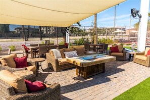 Un patio al aire libre con mobiliario de mimbre, una mesa de centro de madera y un toldo grande que proporciona sombra.