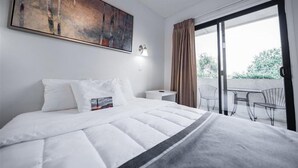 Una habitación de hotel con cama, un cuadro, una mesita de noche, una lámpara y un balcón con sillas.