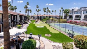 Ein Golfplatz mit Putting Green, Tennisplatz und einer Terrasse mit Außenmöbeln.