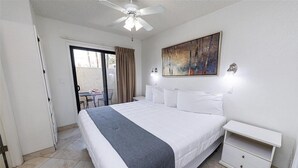 Ein Hotelzimmer mit Bett, Nachttisch, einem Gemälde und einem Deckenventilator.