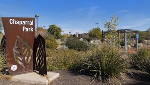 Une porte en métal sur laquelle on peut lire « Chaparral Park », entourée de différentes plantes et surplombée par un ciel bleu clair.